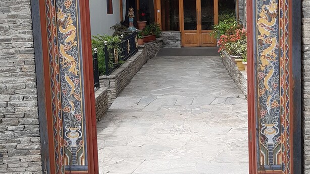 A traditional building entrance with ornate carvings and a stone pathway leading to a wooden door. - Kisa Villa (Thimphu)