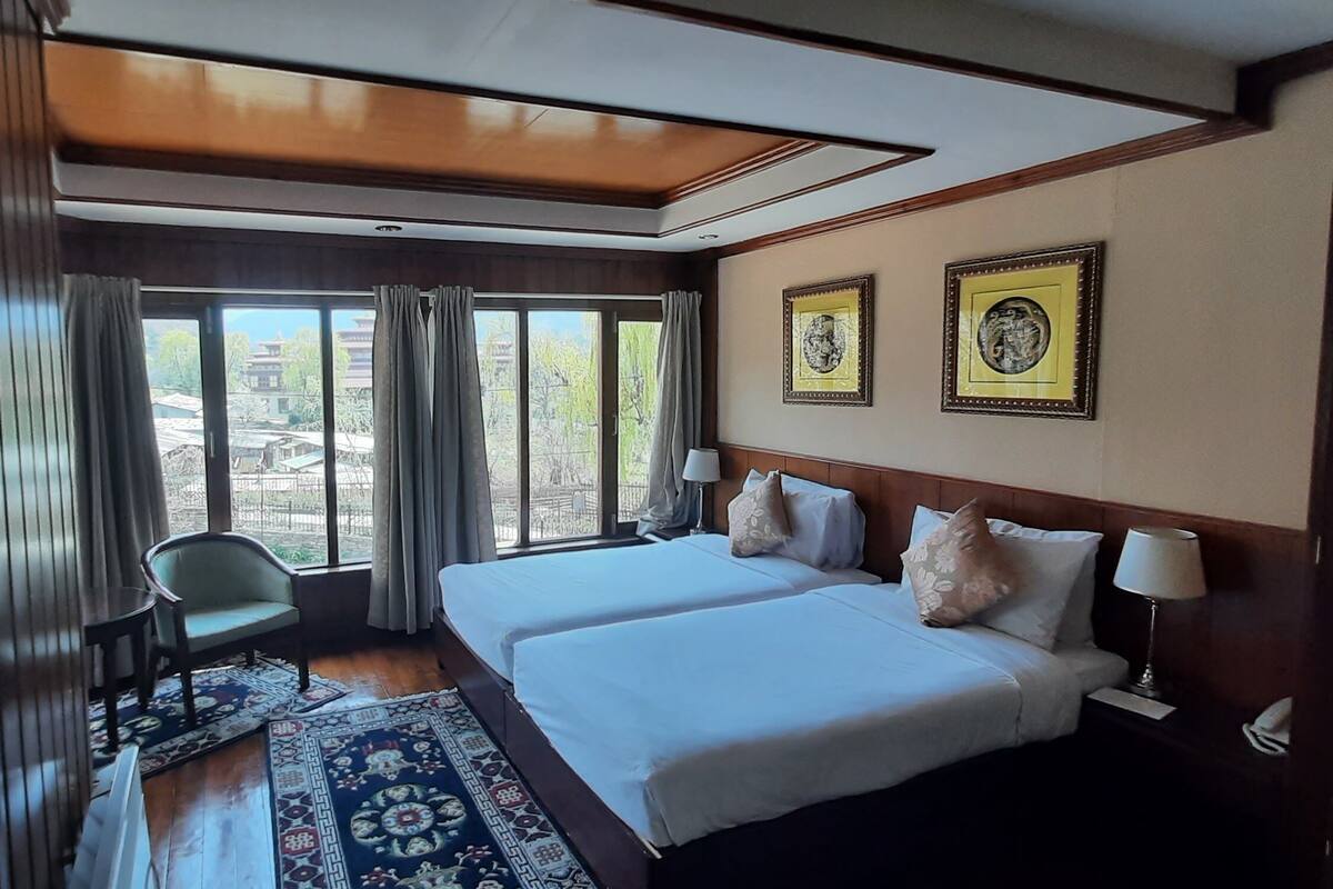 A hotel room with two beds, a chair, a window with curtains, and a view of the outside.