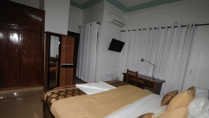 A hotel room with a bed, a desk, a chair, a wardrobe, and a TV mounted on the wall. - Résidence Georges VI (Ouagadougou)