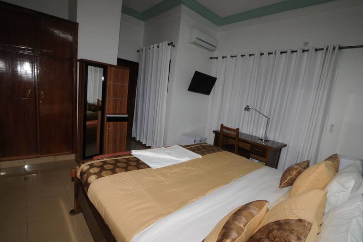 A hotel room with a bed, a desk, a chair, a wardrobe, and a TV mounted on the wall.