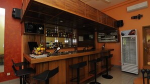 A bar area with wooden bar counter, black bar stools, a refrigerator, and shelves with bottles and glasses. - Résidence Georges VI (Ouagadougou)