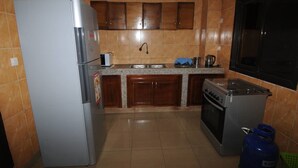 A kitchen with a refrigerator, stove, sink, and wooden cabinets. - Résidence Georges VI (Ouagadougou)