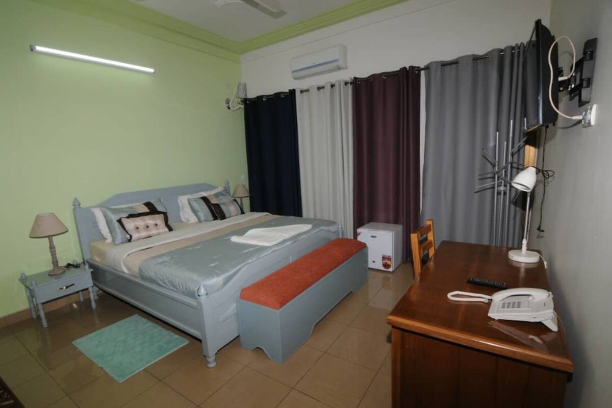 A bedroom with a bed, bedside table, lamp, and a desk with a telephone.