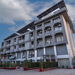 Un hotel de varios pisos con balcones, paneles solares y un patio empedrado.