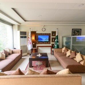 A living room with two sofas, a coffee table, a TV, and flags. - Hotel One Jinnah (Islamabad)