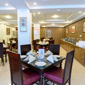 A dining area with a central table set for four, surrounded by chairs with red cushions. - Hotel One Jinnah (Islamabad)