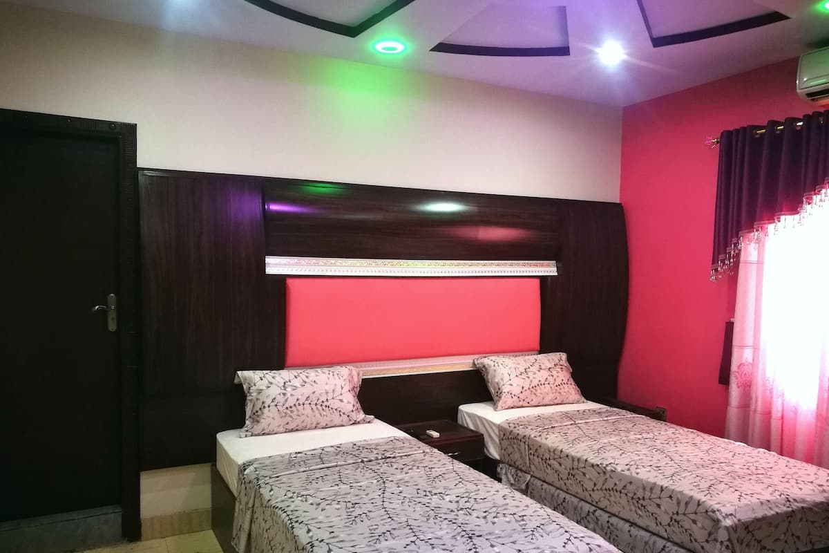 A room with two single beds, a red accent wall, a ceiling with recessed lighting, and a door.