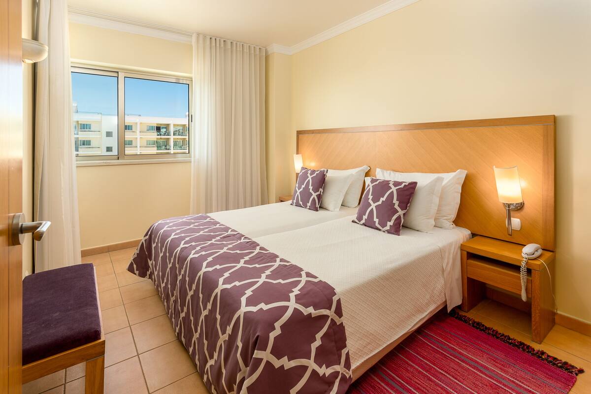 A hotel room with a large bed, two bedside tables, a chair, and a window with curtains.