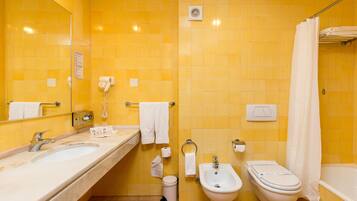 A bathroom with yellow tiled walls, a sink, a bidet, a toilet, a shower curtain, and a mirror.