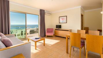 A modern hotel room with a balcony, a sofa, a dining table, and a TV.