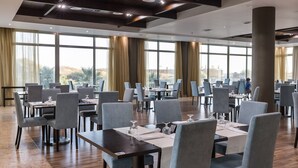 A spacious dining area with multiple tables and chairs, large windows, and a modern ceiling design. - Hotel Apartamentos Dunamar (Vila Real Santo Antonio)