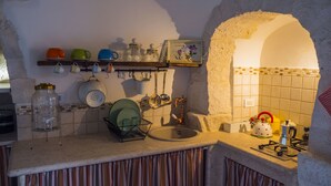 Une cuisine avec une arche en pierre, un évier, ainsi que divers ustensiles de cuisine et de la vaisselle sur le plan de travail.