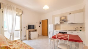 A compact hotel room with a bed, a dining table with chairs, a kitchenette, and a television. - Case Vacanza Rivabella (Gallipoli)