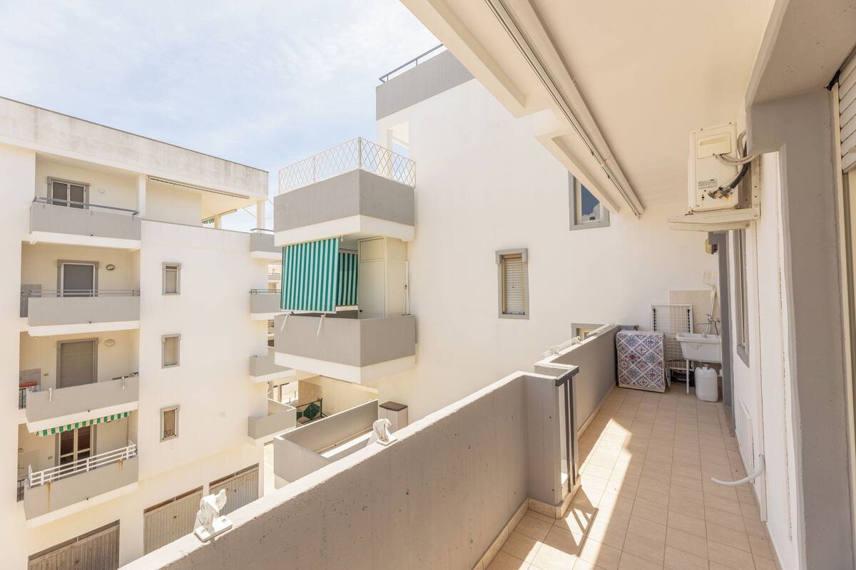 A multi-story residential building with balconies, a visible laundry area, and a window with a towel hanging outside.