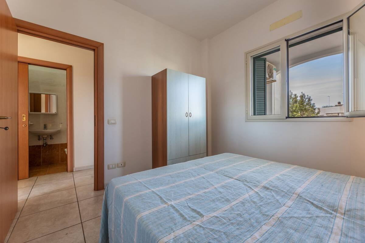 A bedroom with a bed, a wardrobe, a window with a view, and a bathroom with a mirror and sink.