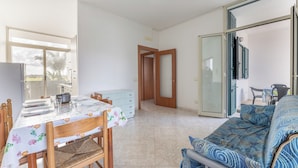 A dining area with a table set for four, a sofa, and a sliding glass door leading to a balcony. - Case Vacanza Rivabella (Gallipoli)