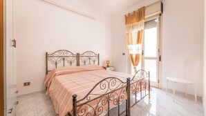 A bedroom with a bed, a nightstand, a chair, and a window with curtains. - Case Vacanza Rivabella (Gallipoli)