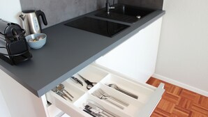 A modern kitchen with a black countertop, a built-in sink, and a drawer with utensils. - Hometown-Apartments (Heidelberg)