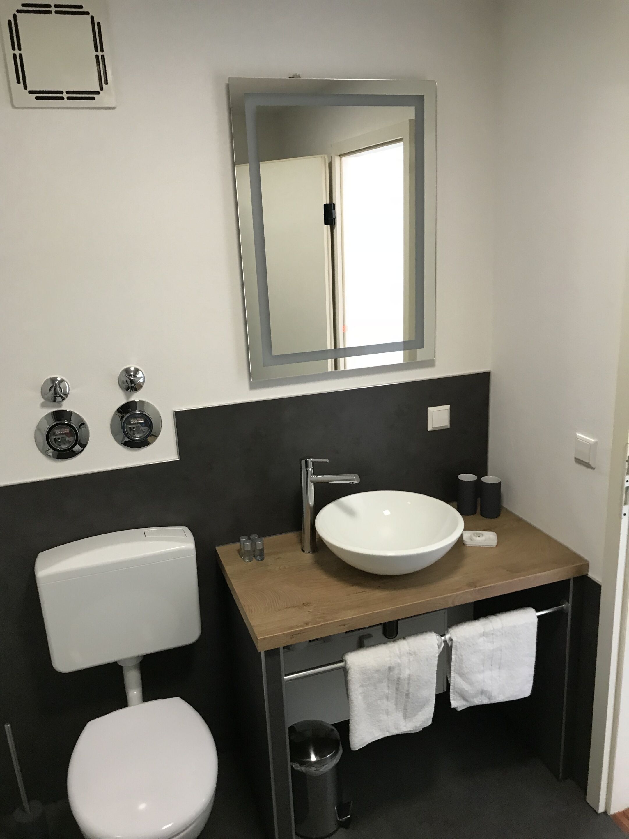 A modern bathroom with a white toilet, a wooden vanity with a white sink, a mirror above the sink, and a towel rack with two towels.