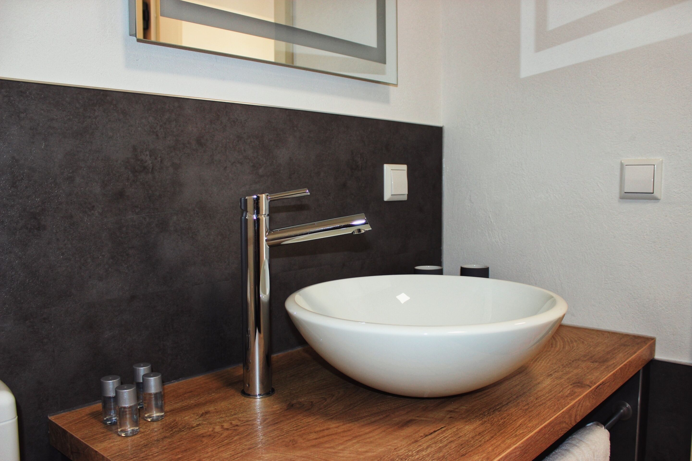 A modern bathroom with a large white vessel sink, a sleek chrome faucet, and a wooden countertop.