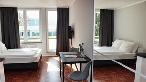 A hotel room with two beds, a dining table, a chair, and a TV. - Hometown-Apartments (Heidelberg)