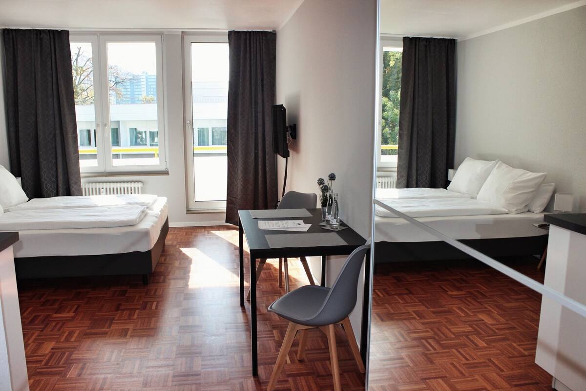 A hotel room with two beds, a dining table, a chair, and a TV.