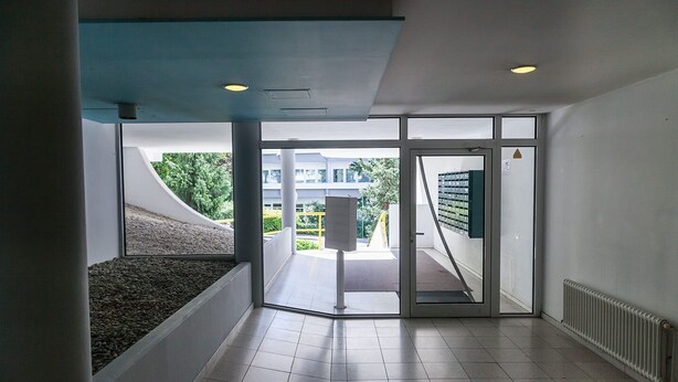 A modern interior with a glass door leading to an outdoor area, tiled flooring, and a visible outdoor view. - Hometown-Apartments (Heidelberg)