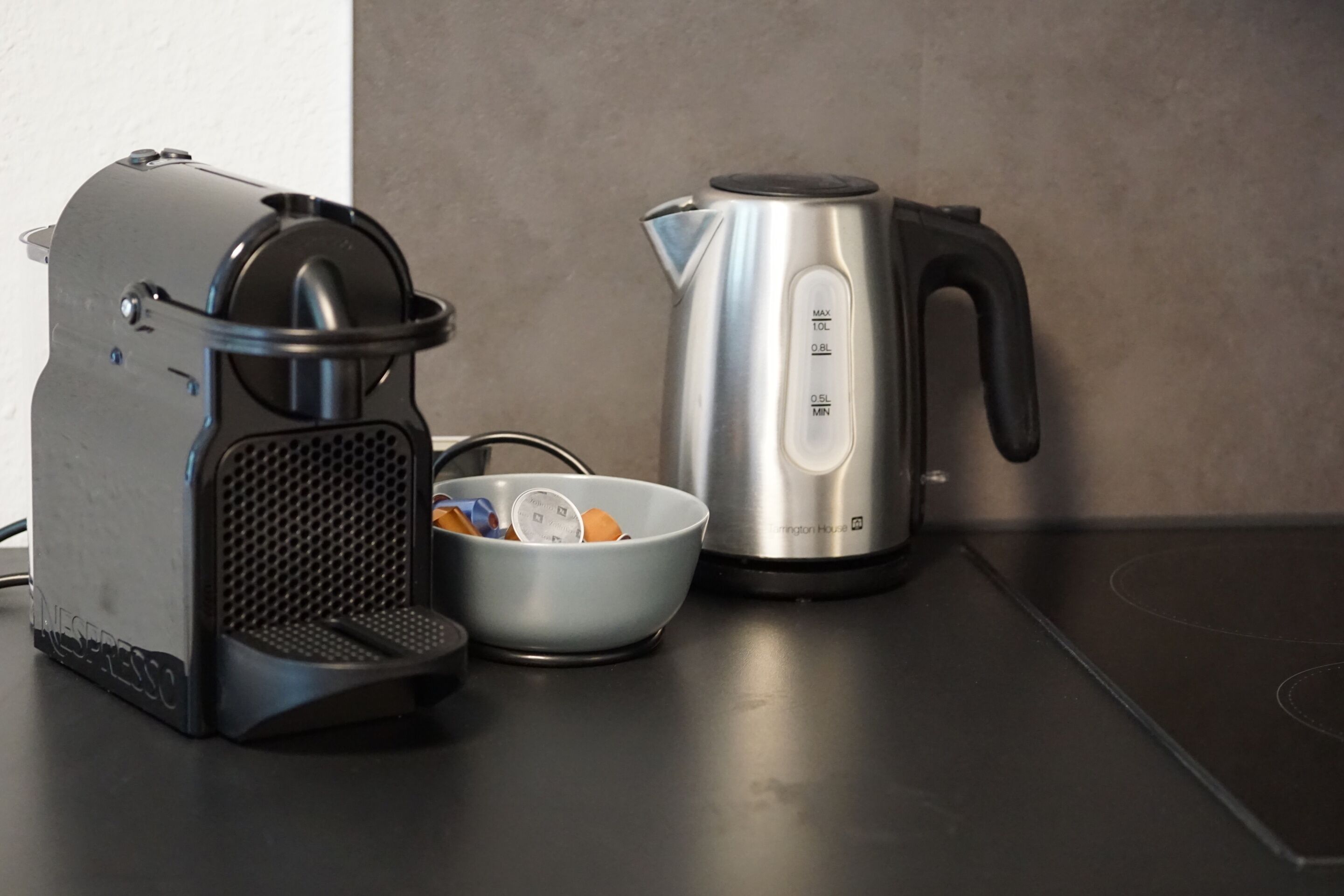 A kitchen with a coffee maker, a kettle, and a bowl with items.