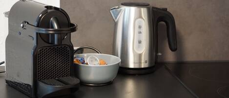 Una cocina con cafetera, hervidor y un bol con objetos.