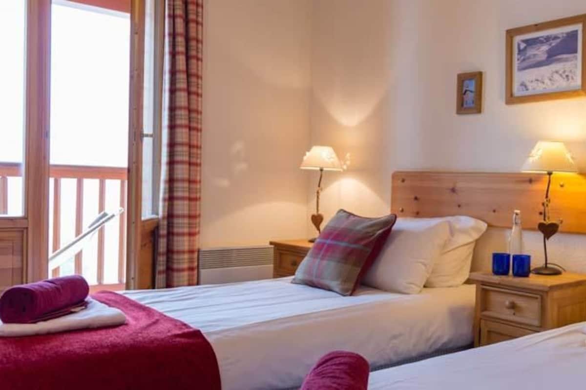 Une chambre d’hôtel avec deux lits, une tête de lit en bois, des tables de chevet avec des lampes et un balcon doté d’une balustrade.