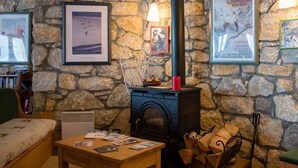 A cozy room with a stone wall, a fireplace, a wooden table, and framed pictures on the wall. - Chalet Cœur des Brévières by Chalet Chardons (Tignes)
