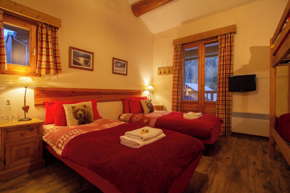 Une chambre d’hôtel avec deux lits, des têtes de lit en bois, une télévision et une fenêtre avec des rideaux.