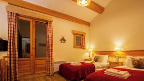 A hotel room with two beds, wooden floors, a wooden ceiling, a small window, and a television on the wall. - Chalet Cœur des Brévières by Chalet Chardons (Tignes)