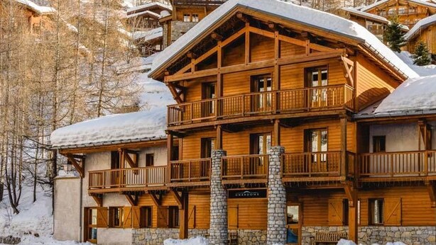 A multi-story wooden lodge with balconies and a stone foundation, surrounded by snow-covered trees. - Chalet Cœur des Brévières by Chalet Chardons (Tignes)