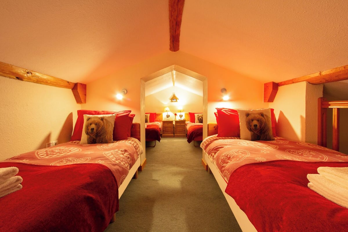 Une chambre confortable avec deux lits, chacun agrémenté d’un oreiller en forme d’ours en peluche, et un luminaire central.
