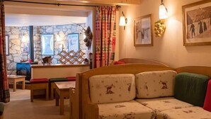 A cozy room with a wooden bench, a sofa with patterned cushions, and a stone wall. - Chalet Cœur des Brévières by Chalet Chardons (Tignes)