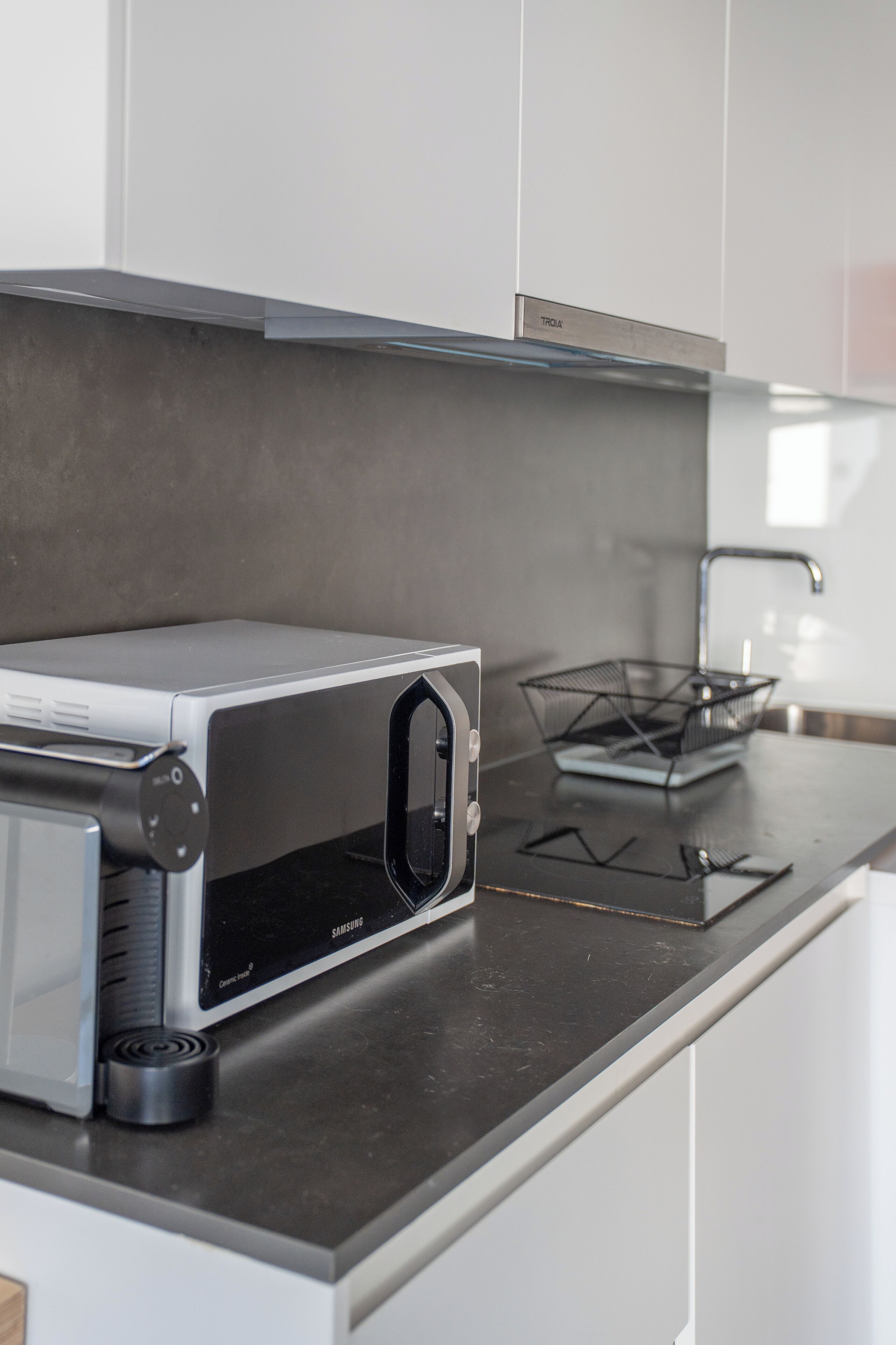 A modern kitchen with a built-in microwave, a kettle, and a black tray on the countertop.