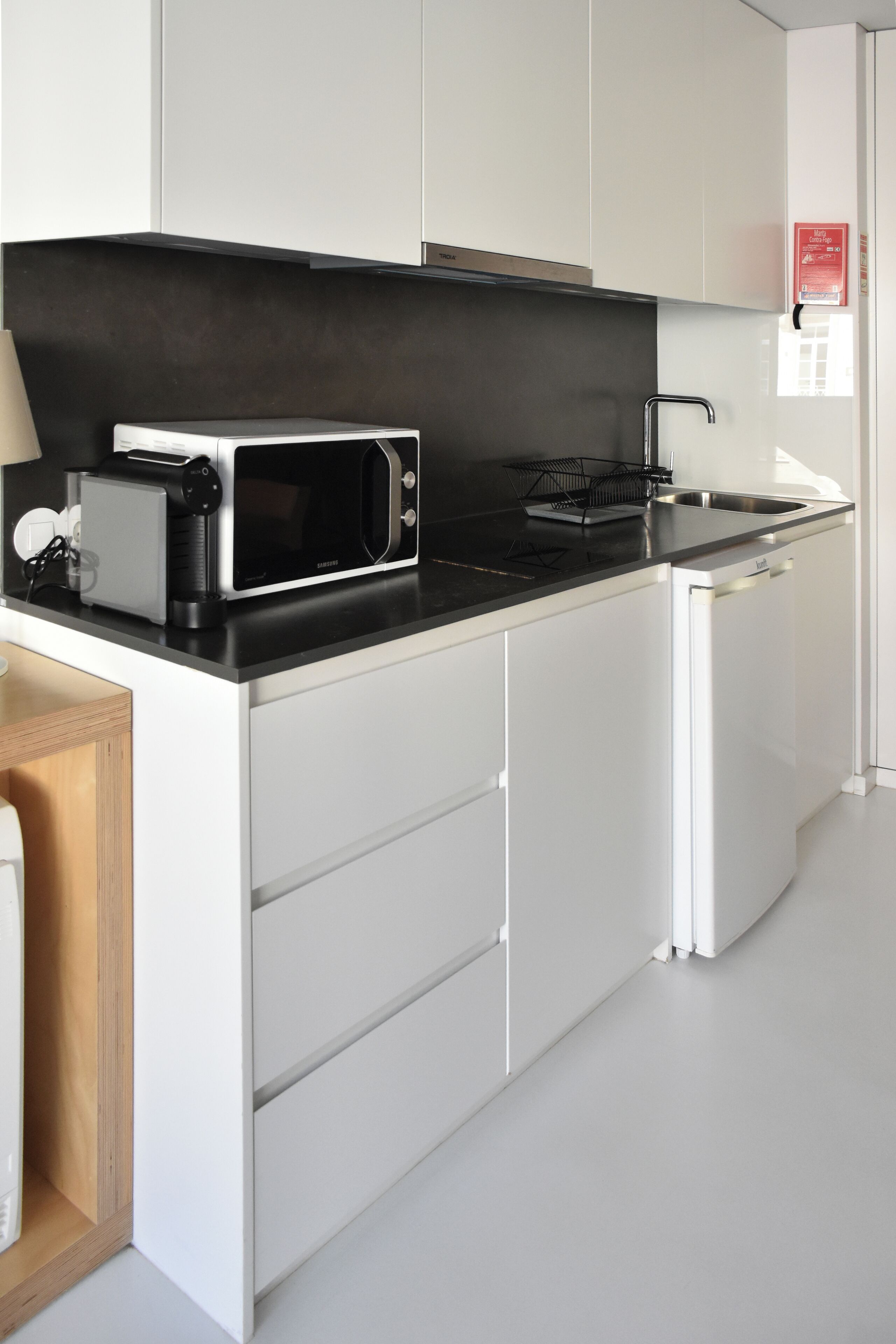 Una cocina moderna con armarios blancos, encimera negra, microondas y un refrigerador pequeño.