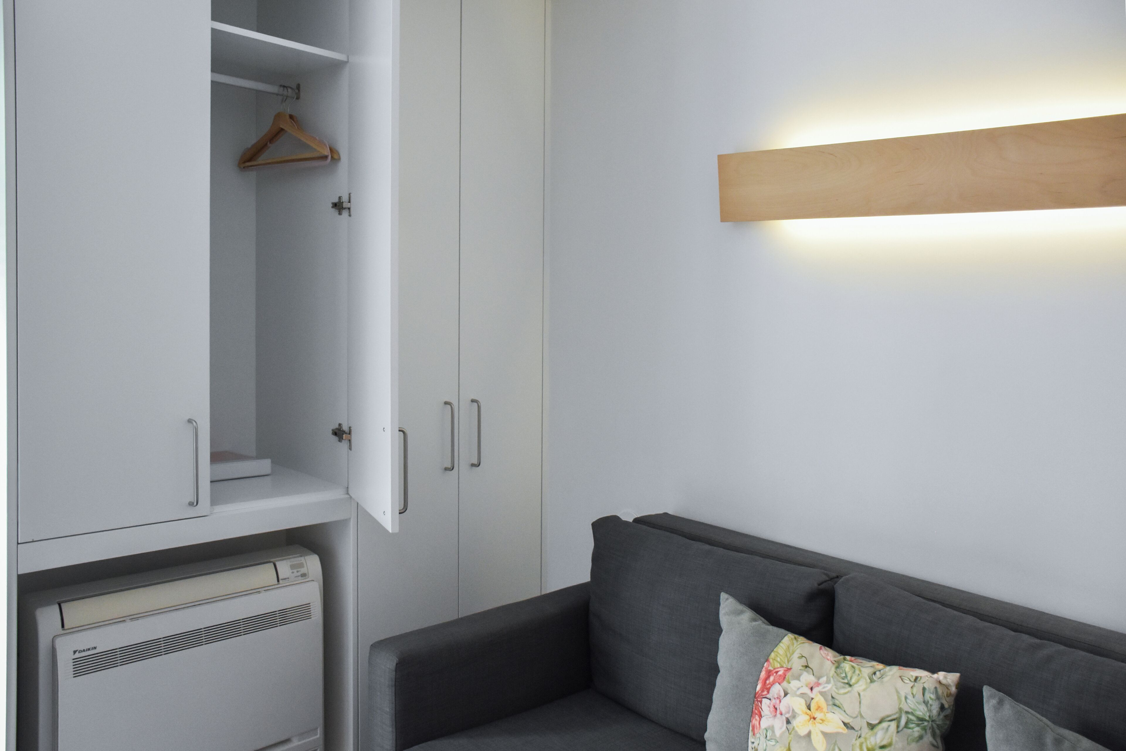 Una habitación con un sofá gris, un armario blanco y una lámpara fijada a la pared.