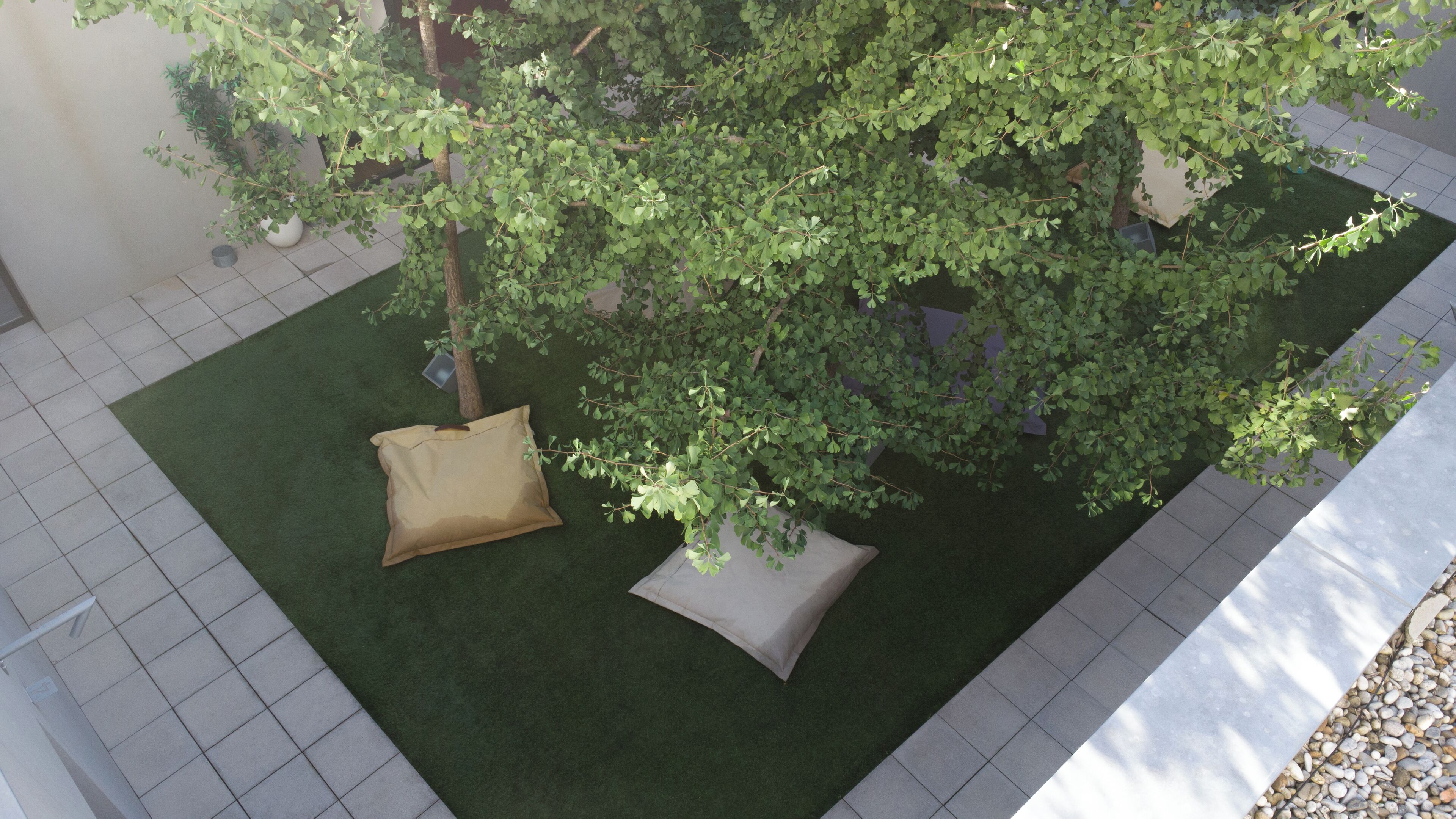 A courtyard with artificial grass, two beige cushions, and a tree.