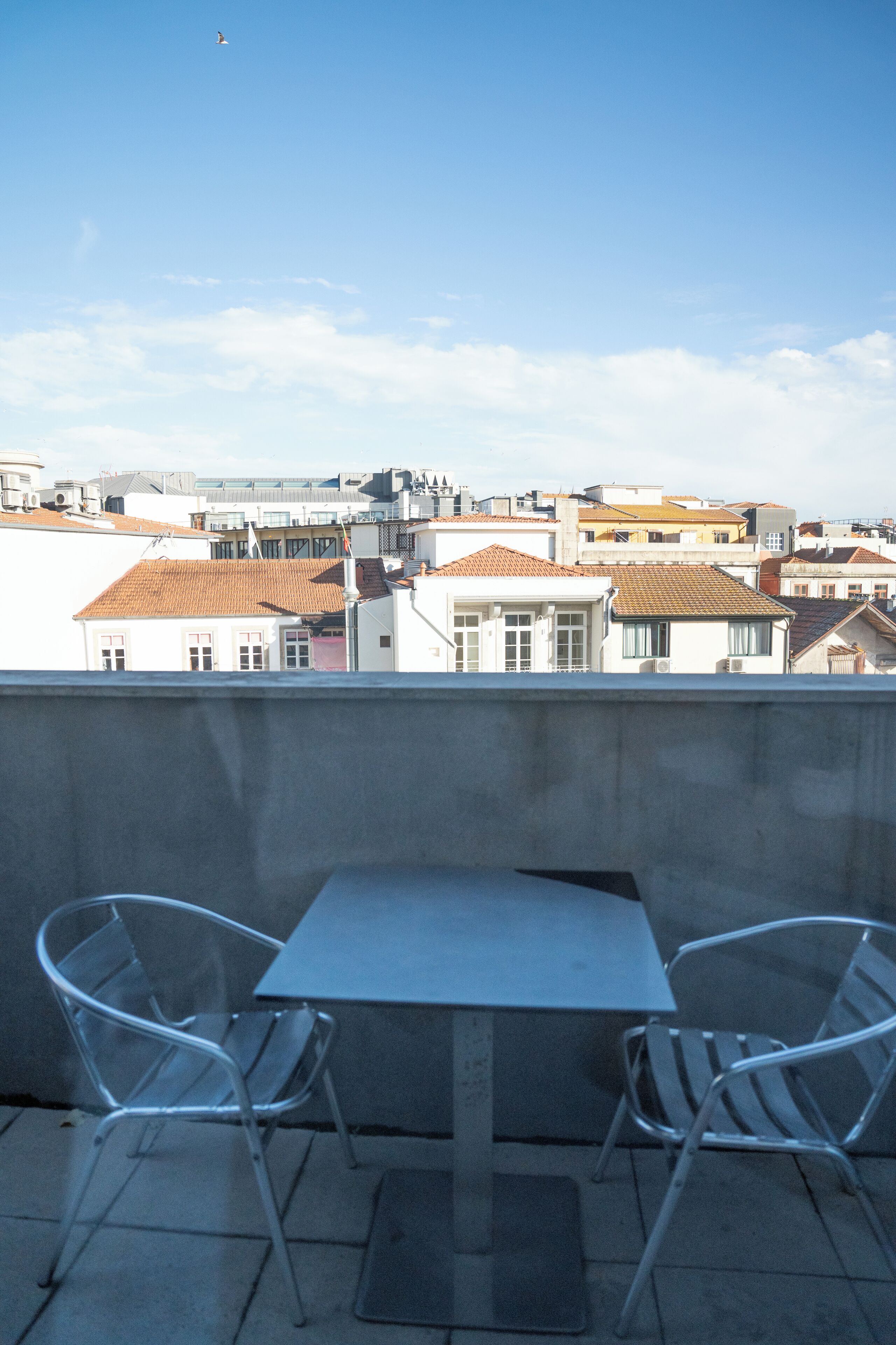 Une terrasse avec une table et deux chaises, d’où l’on peut admirer un paysage urbain avec ses bâtiments et un ciel dégagé.