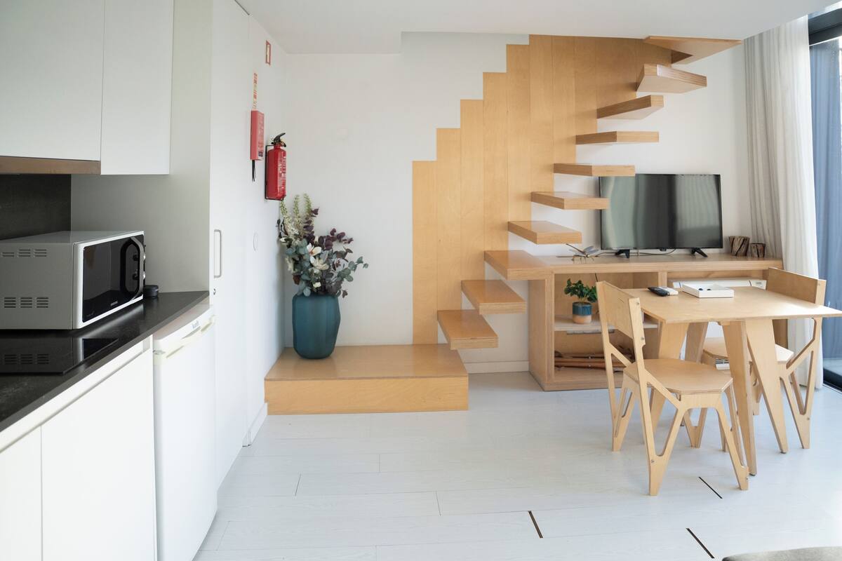 Eine moderne Küche mit Mikrowelle, einer Blumenvase und einer Holztreppe, die in einen Essbereich mit Tisch und Stühlen führt.