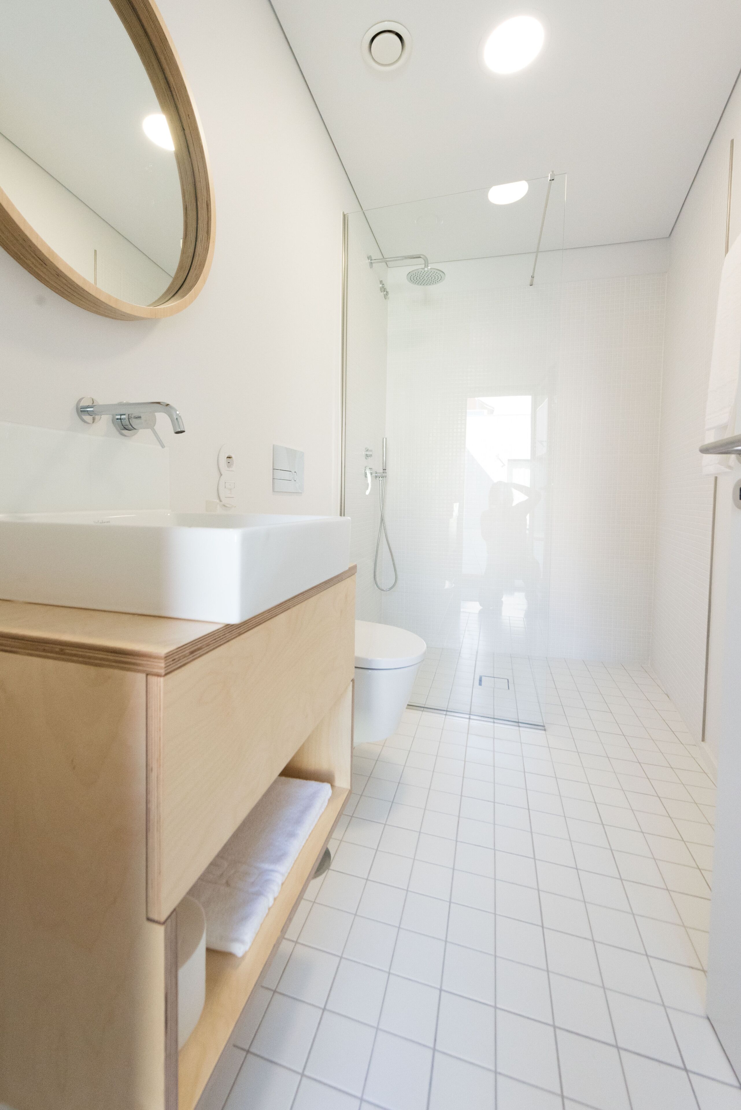A modern bathroom with a wooden vanity, a large mirror, a white sink, and a shower area.