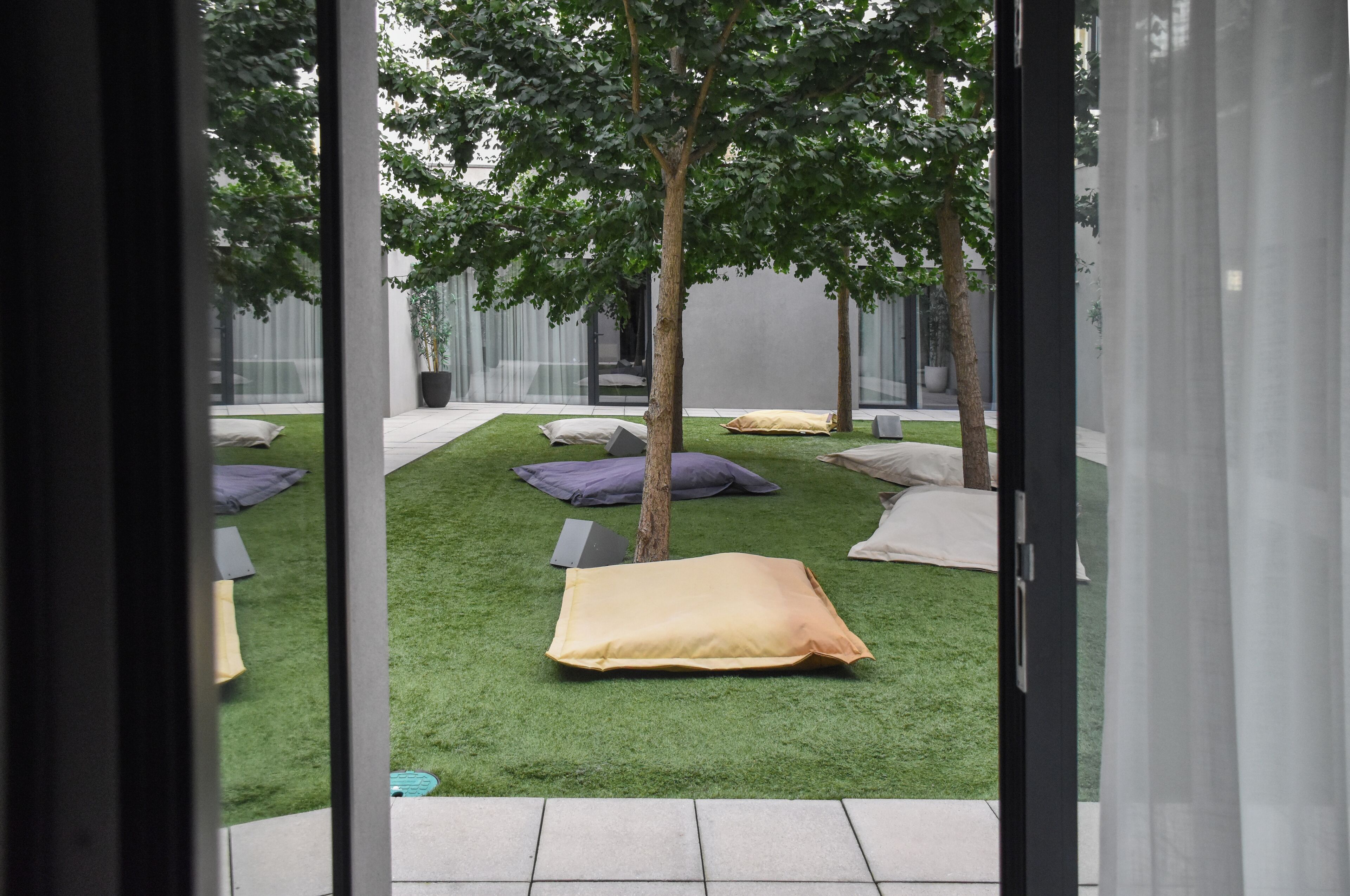 A modern outdoor relaxation area with artificial grass, several pillows, and a tree.