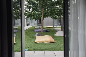 A modern outdoor relaxation area with artificial grass, several pillows, and a tree. - I Loft Porto (Porto)