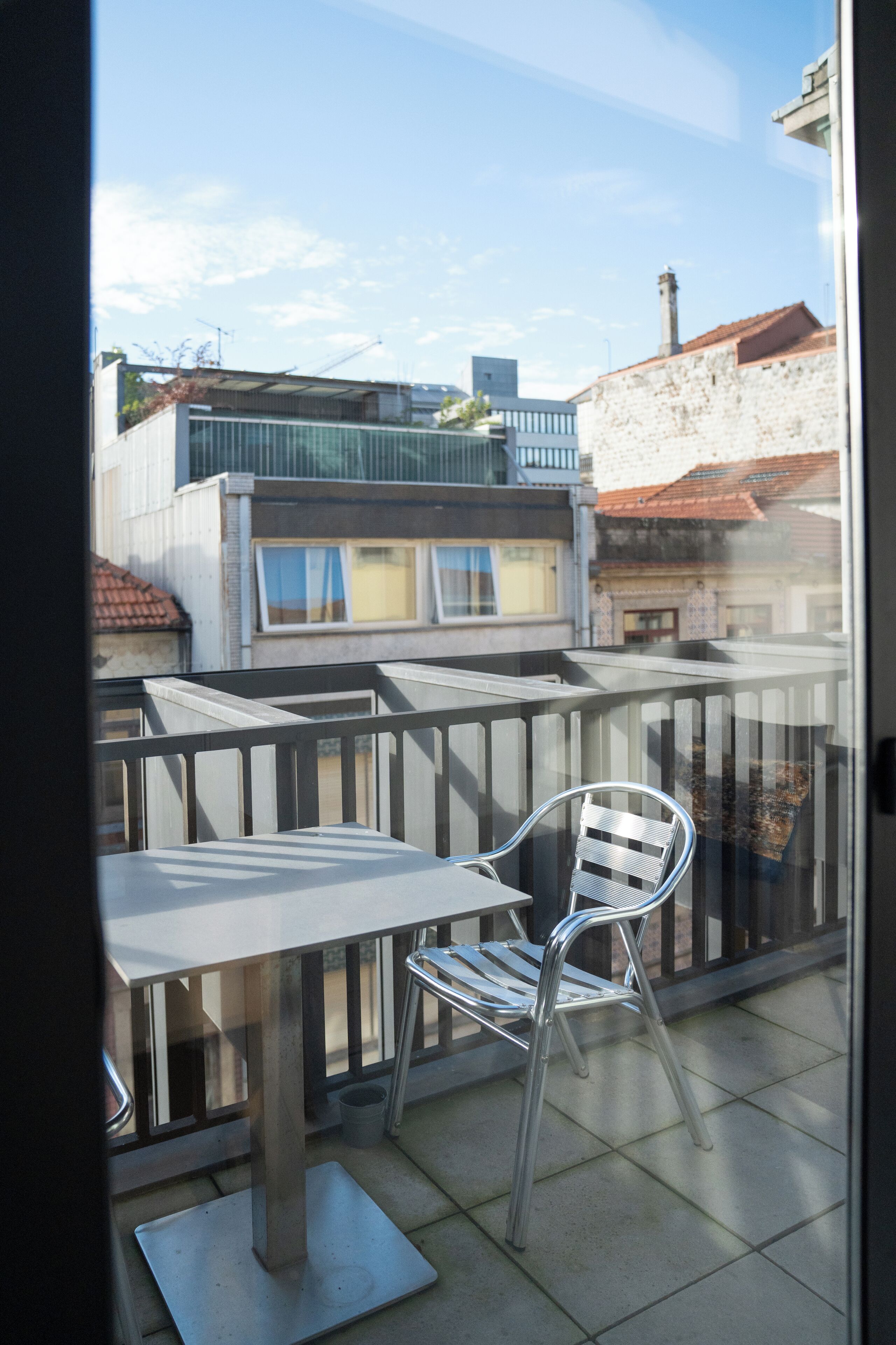 A balcony with a metal table and chair, a view of buildings, and a clear sky.