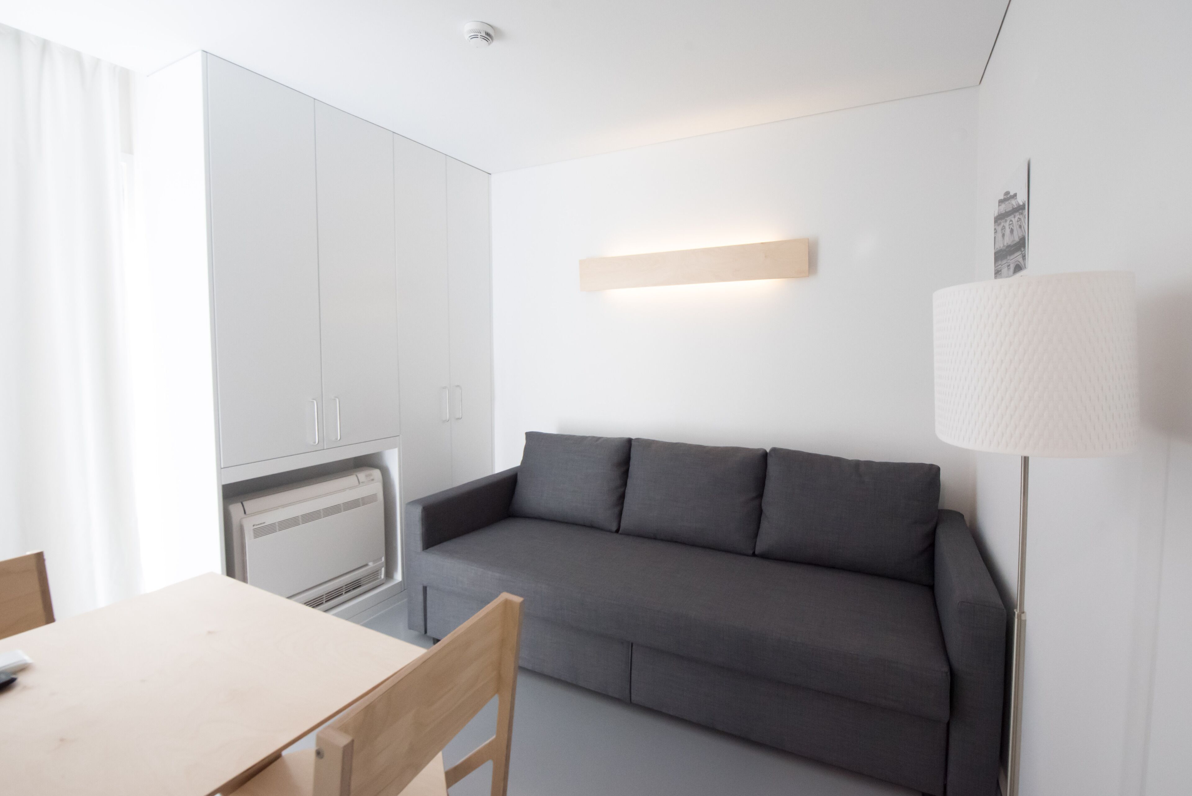 Una habitación moderna y minimalista con un sofá gris, una mesa de comedor de madera y un radiador blanco.