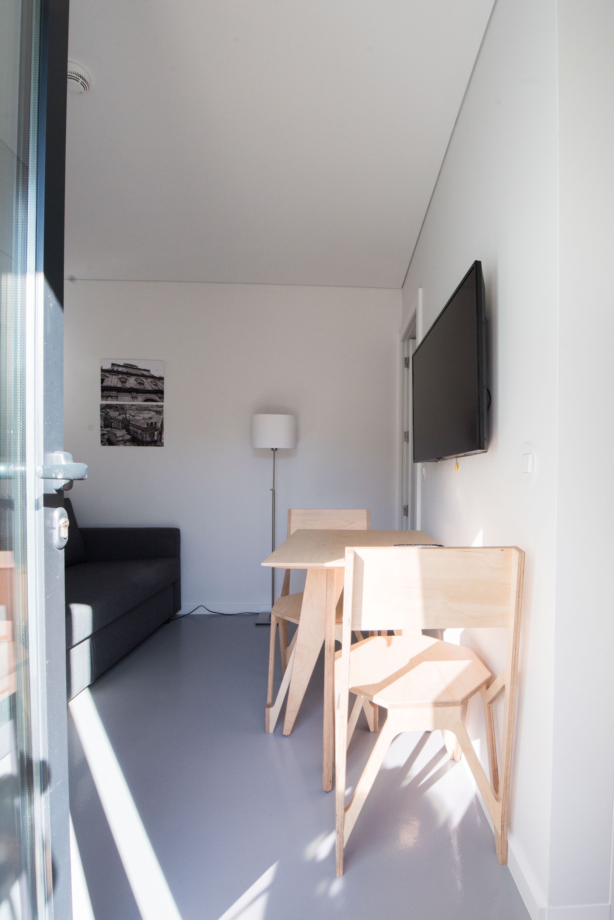 Un soggiorno moderno con un divano, un tavolo da pranzo in legno con sedie, una TV a schermo piatto montata a parete e una lampada da terra.