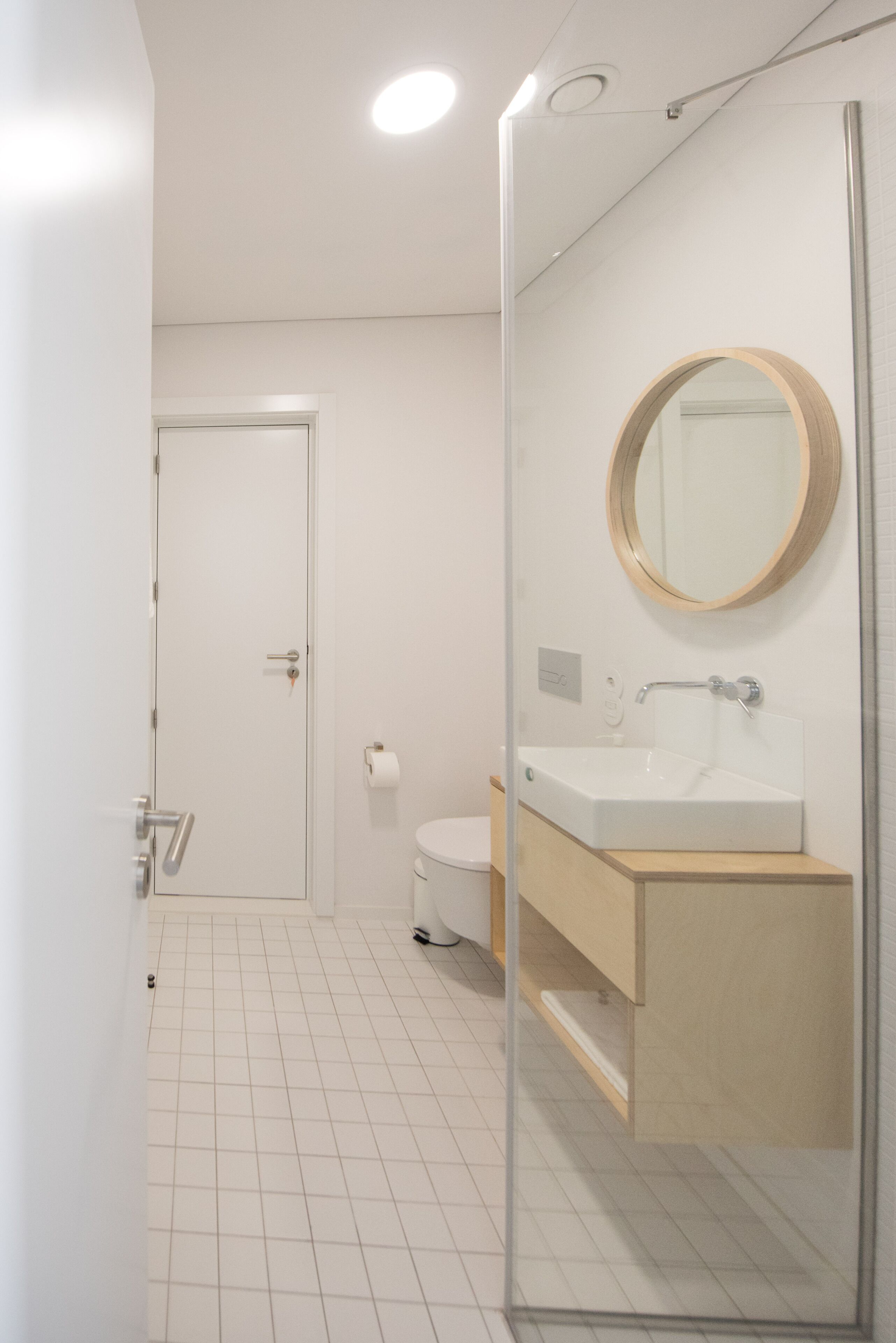 A modern bathroom with a glass shower enclosure, a white toilet, and a wooden vanity with a mirror.