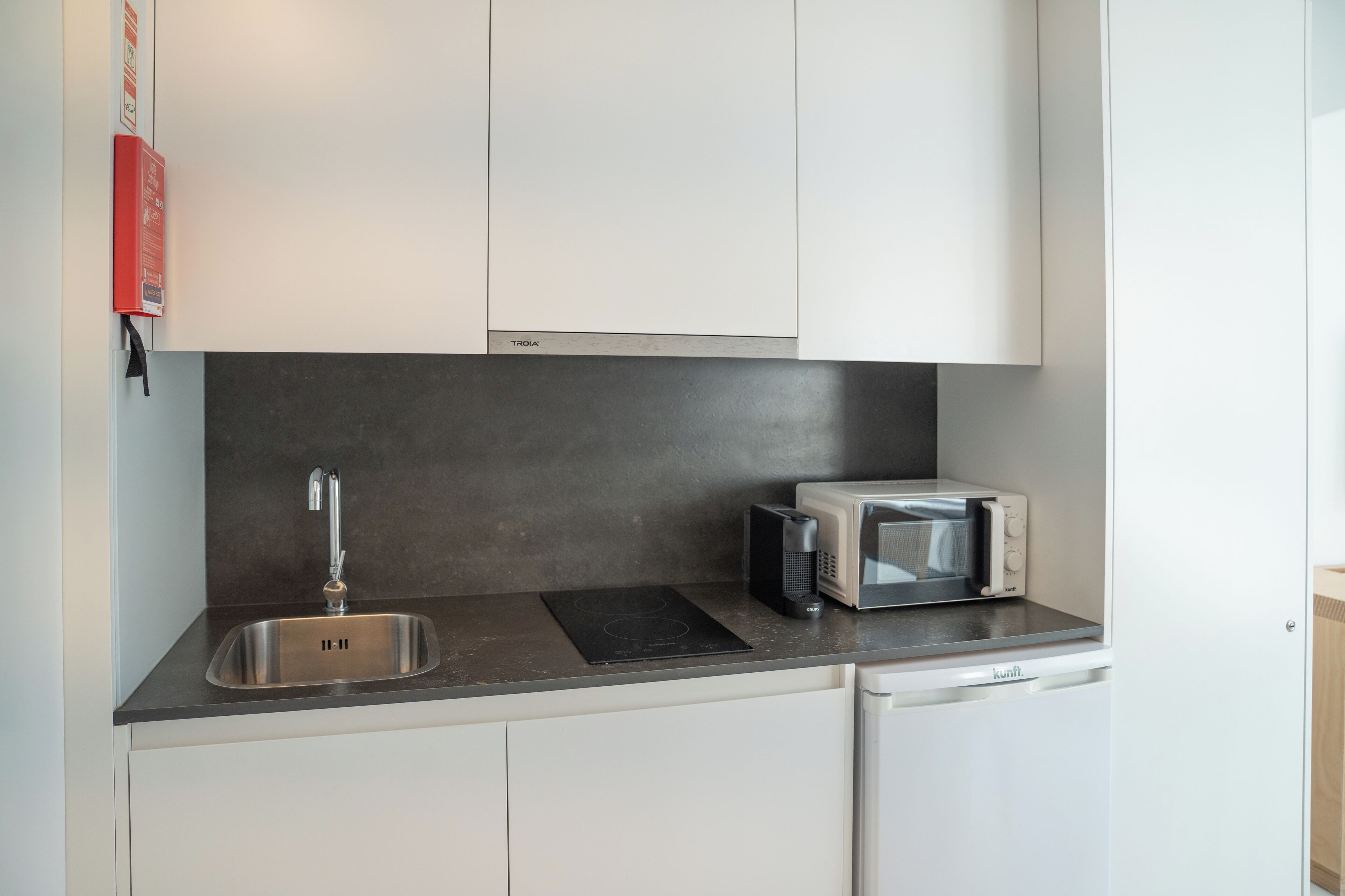 Una cocina moderna con un lavamanos de acero inoxidable, una placa de inducción negra, un microondas y un lavavajillas.